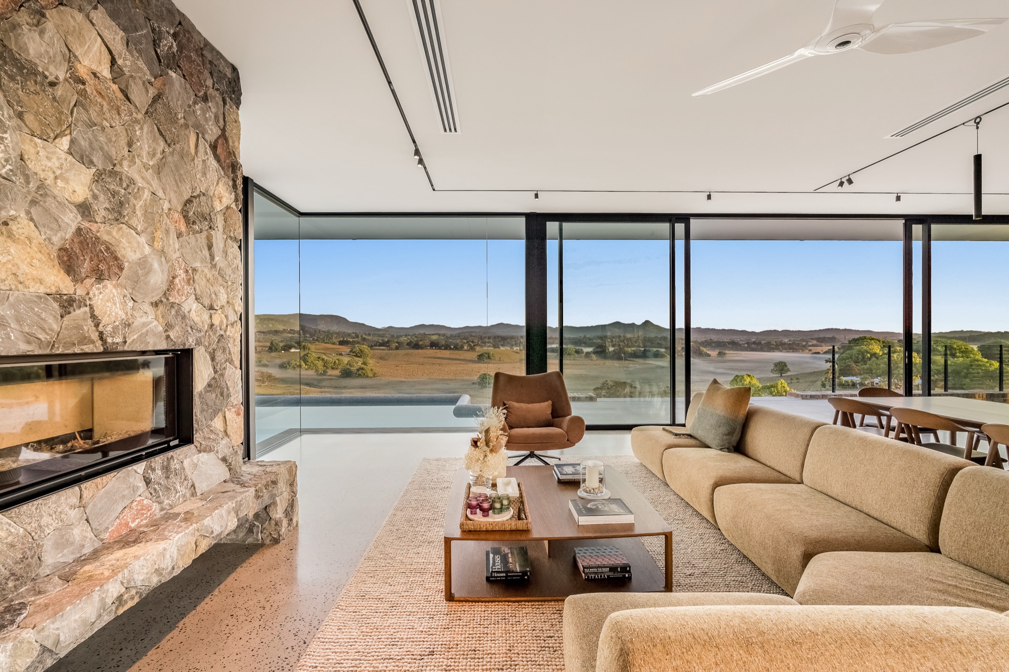 Living room with stone fireplace wall and panoramic mountain views through floor-to-ceiling glass